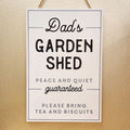 Rustic wooden hanging sign reading “Dad’s Garden Shed” with decorative design and rope hanger.