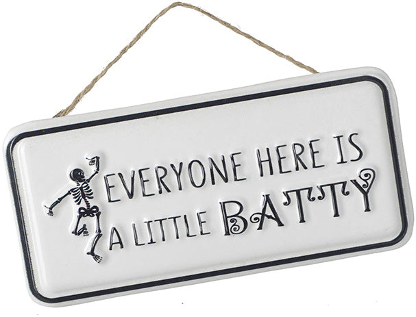 White rectangular metal hanging sign with the phrase "Everyone Here Is A Little Batty" and a dancing skeleton illustration on the left.