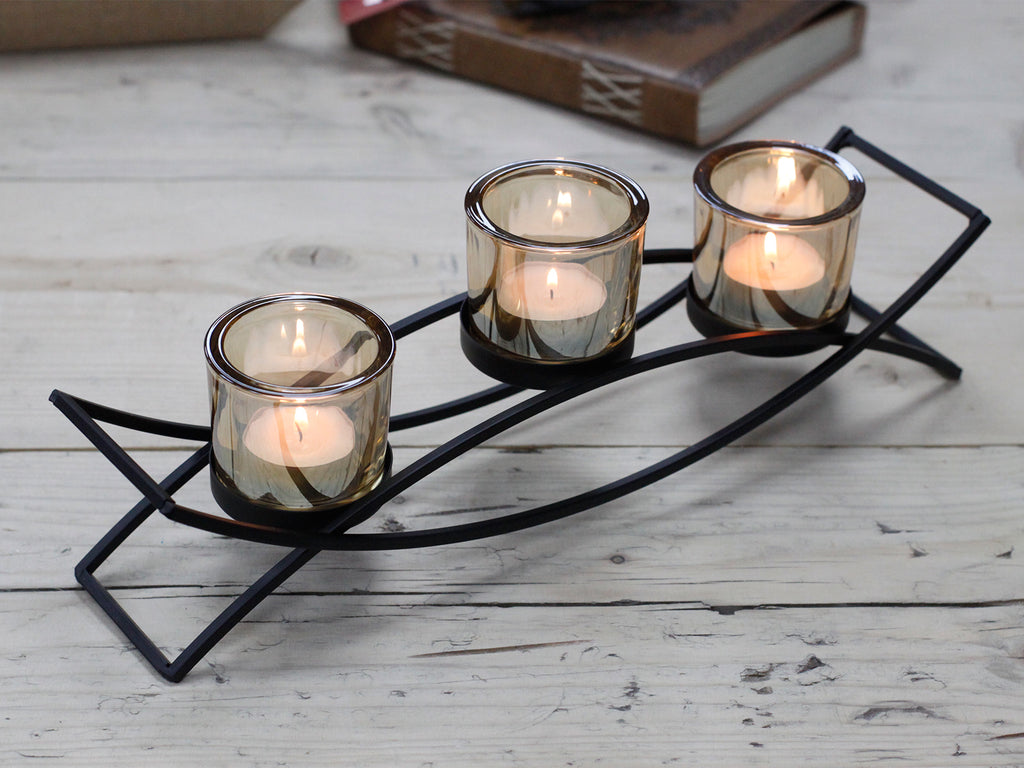 Black iron arch centrepiece candle holder with three amber glass votive cups on a rustic wooden surface