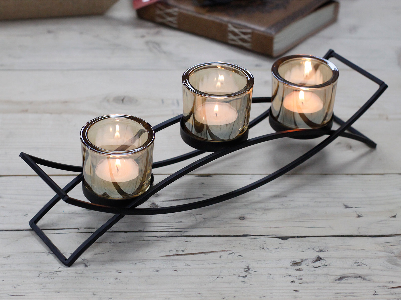 Black iron arch centrepiece candle holder with three amber glass votive cups on a rustic wooden surface