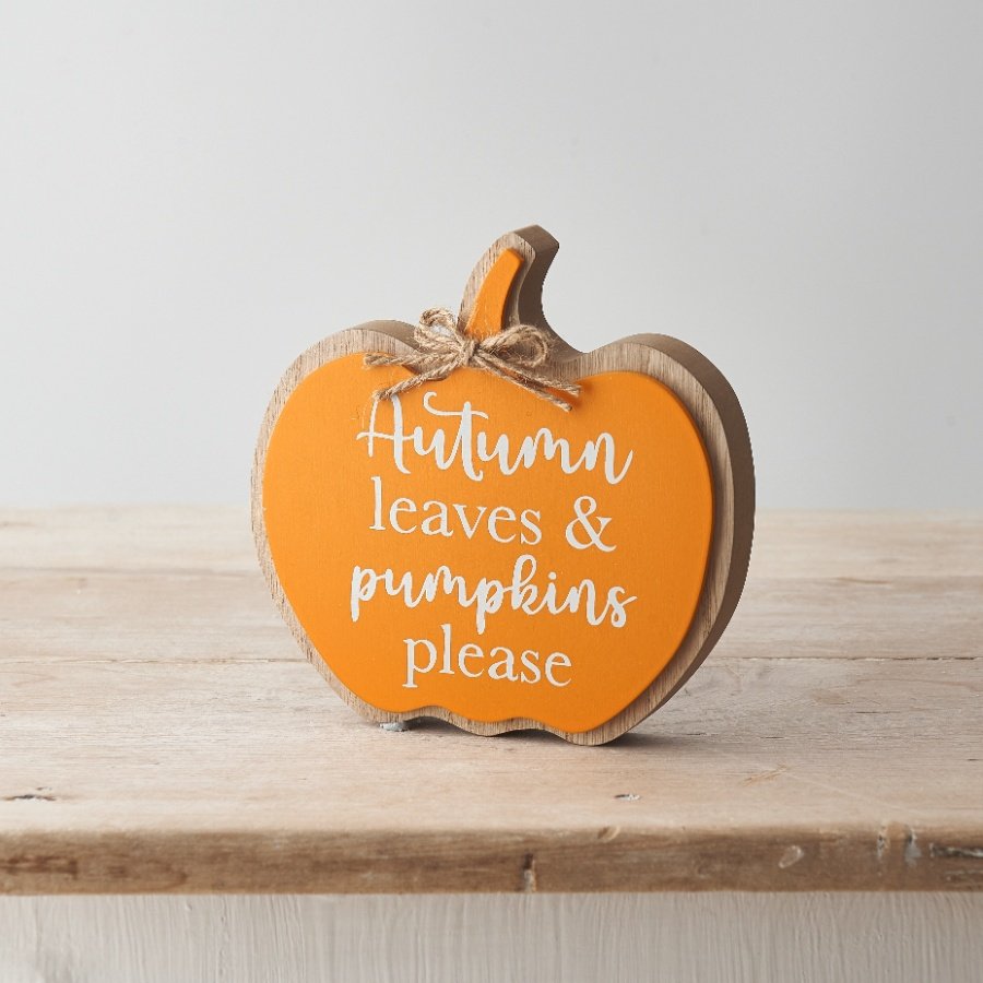 Orange and wood pumpkin shaped block plaque with Autumn Leaves and Pumpkins Please in white script lettering and a twine bow, displayed on a pale wooden surface