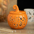 Orange ceramic pumpkin oil burner and wax warmer with folk-inspired cut-out floral and star details, featuring a decorative curled lid.
