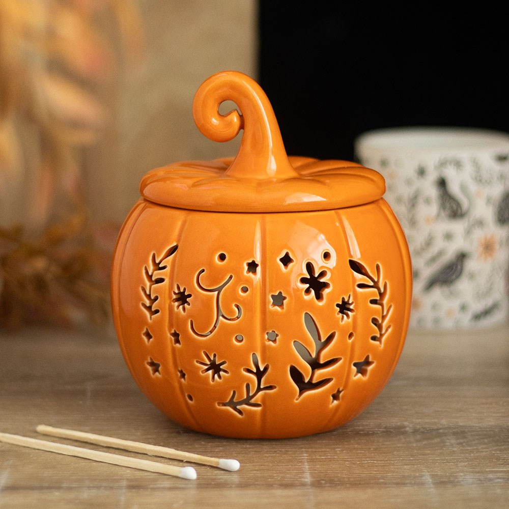 Orange ceramic pumpkin oil burner and wax warmer with folk-inspired cut-out floral and star details, featuring a decorative curled lid.