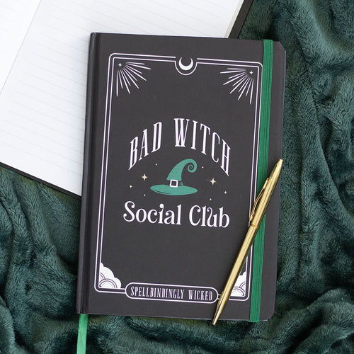Dark hardback A5 notebook with Bad Witch Social Club design, teal green witch hat illustration and Spellbindingly Wicked text, styled on a green fluffy blanket with a gold pen
