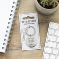 Metal keyring with 'The Best Dad in the World' text on a card, placed on a wooden surface with a keyboard and cactus in the background.