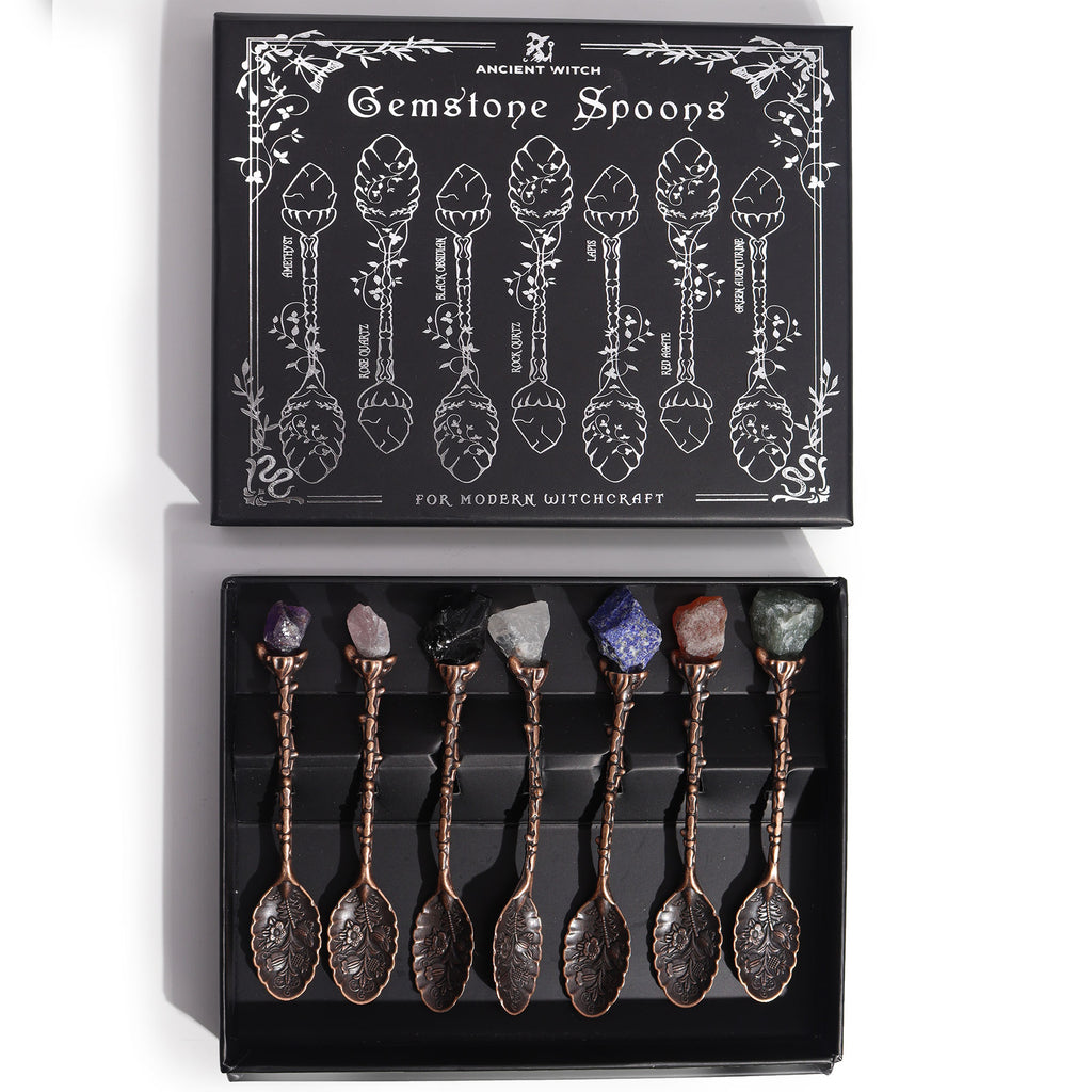 Set of 7 bronze witch spoons with gemstone crystal handles arranged together, mystical themed decorative cutlery set.