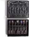 Set of 7 bronze witch spoons with gemstone crystal handles arranged together, mystical themed decorative cutlery set.
