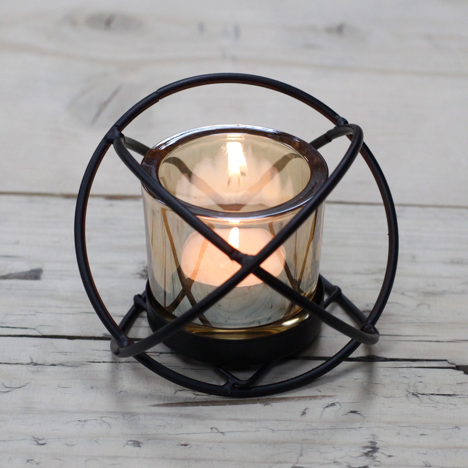 Black iron spherical candle holder with a single amber glass votive cup, on a rustic wooden surface