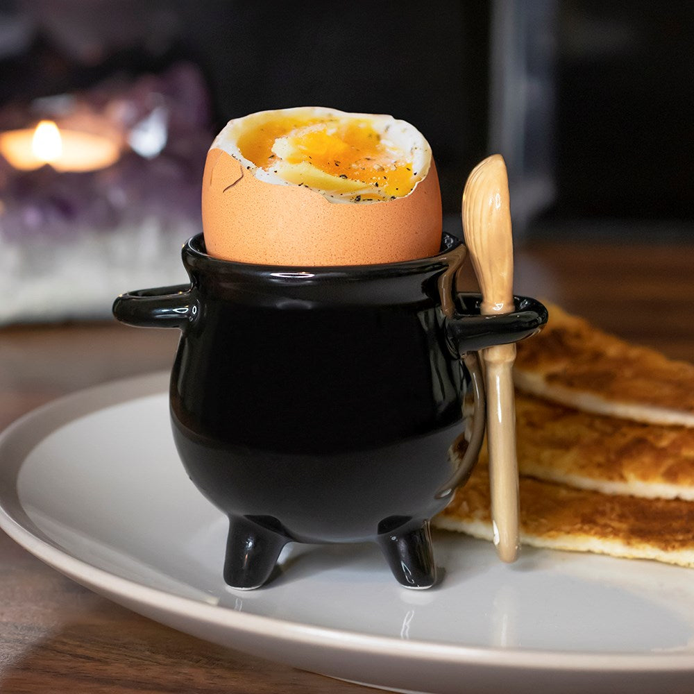 Ceramic cauldron shaped egg cup with miniature broom spoon in magical witch-inspired design.