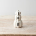 White ceramic stacked pumpkin ornament with "BOO" lettering across three tiers, displayed on a wooden surface

