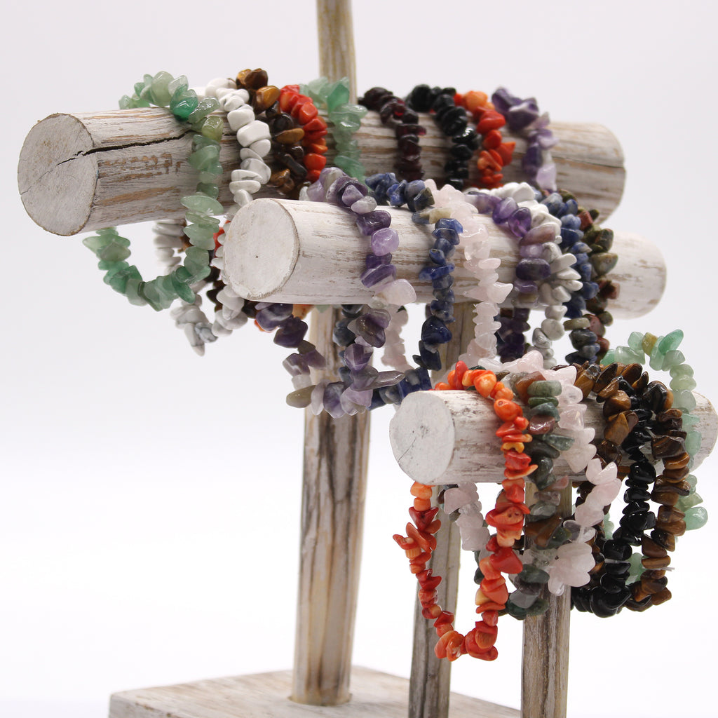 Selection of crystal chipstone bracelets in assorted gemstones, including amethyst, rose quartz and tiger's eye displayed on a wooden stand.