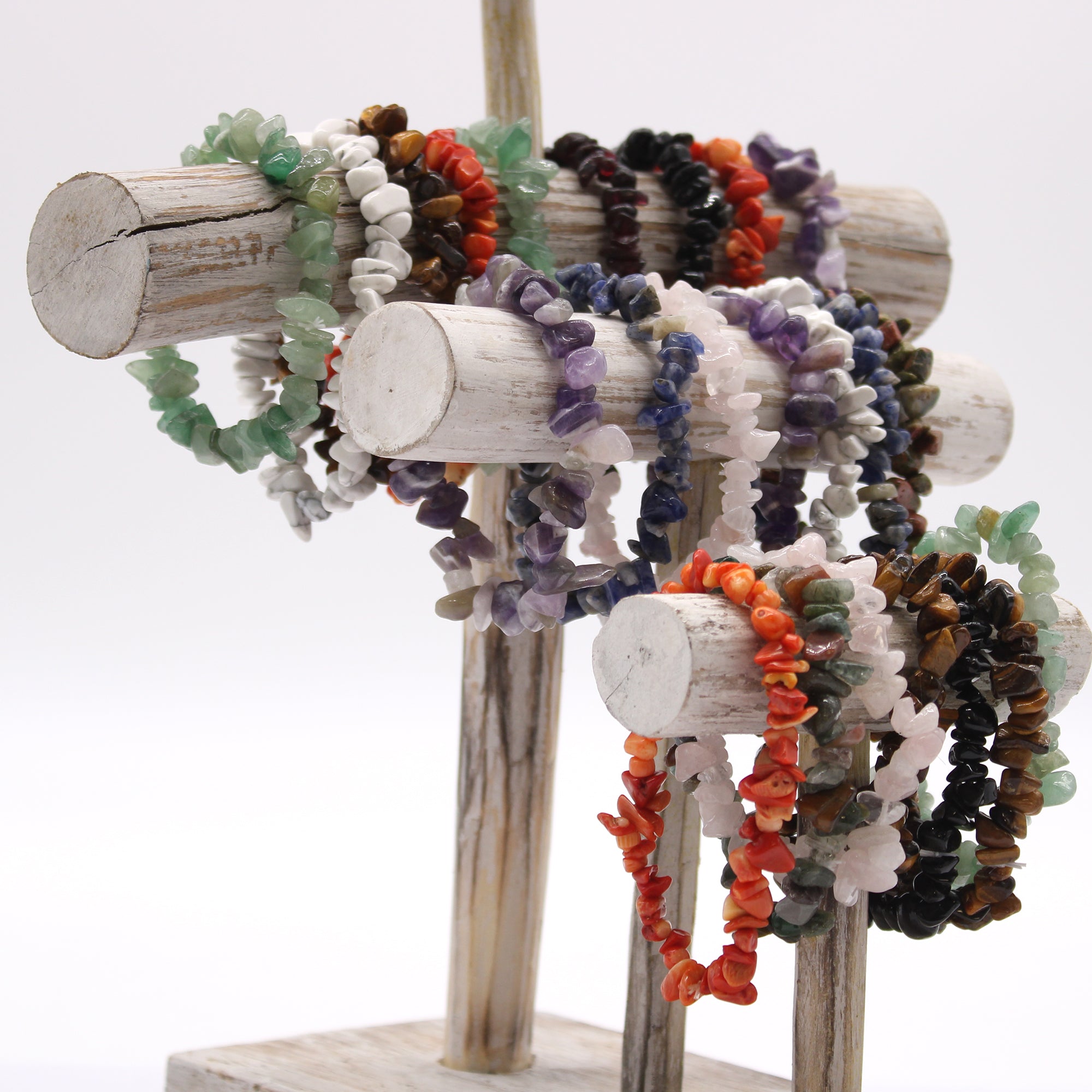 Selection of crystal chipstone bracelets in assorted gemstones, including amethyst, rose quartz and tiger's eye displayed on a wooden stand.