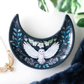 Dark blue ceramic crescent moon shaped trinket dish with a white barn owl in flight design surrounded by blue botanical leaves and white flowers, styled with a gold owl necklace and dark blue velvet fabric
