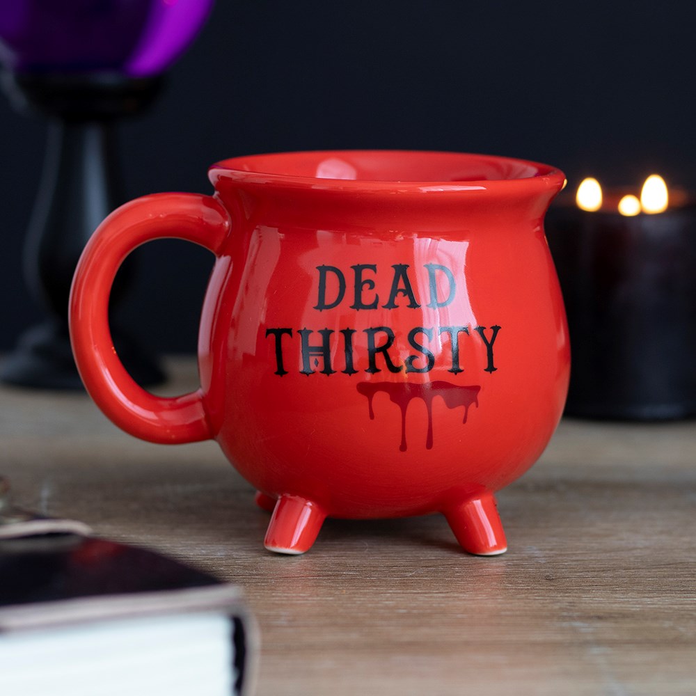 Red ceramic cauldron-shaped mug with 'Dead Thirsty' gothic lettering and drip detail, styled with candles and dark décor