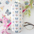 White hard shell glasses case with an all-over floral bug pattern featuring pastel butterflies, bees and ladybirds, styled with pink gypsophila and a pair of glasses