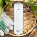 Pale green wooden wall thermometer with "Welcome To My Garden" text, three flower pot illustrations, and dual Celsius and Fahrenheit temperature scale