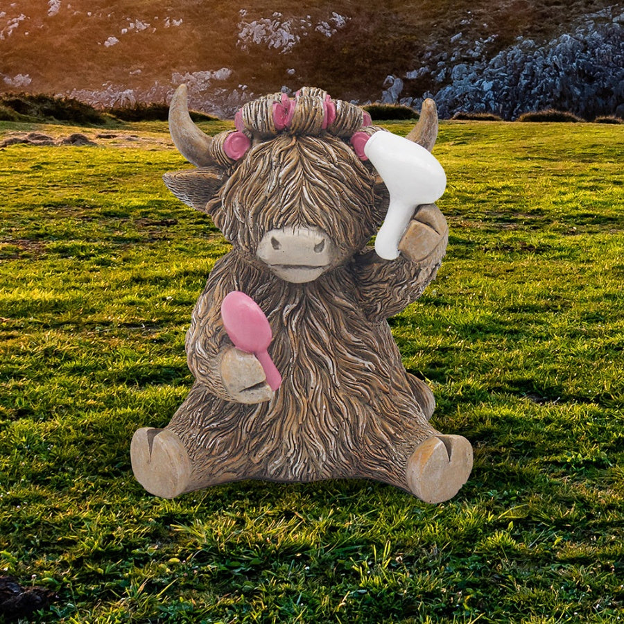 Highland cow resin figurine holding a white hairdryer and pink brush with pink hair rollers, set against a Scottish highland landscape