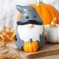 Grey ceramic Halloween gonk oil burner with star-cut witch hat, white beard, orange and black striped scarf, and orange pumpkin, styled with autumn pumpkins and leaves on a wooden board