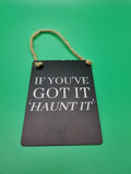 Black mini metal hanging sign with white "If You've Got It Haunt It" slogan and jute rope hanger, photographed against a green background