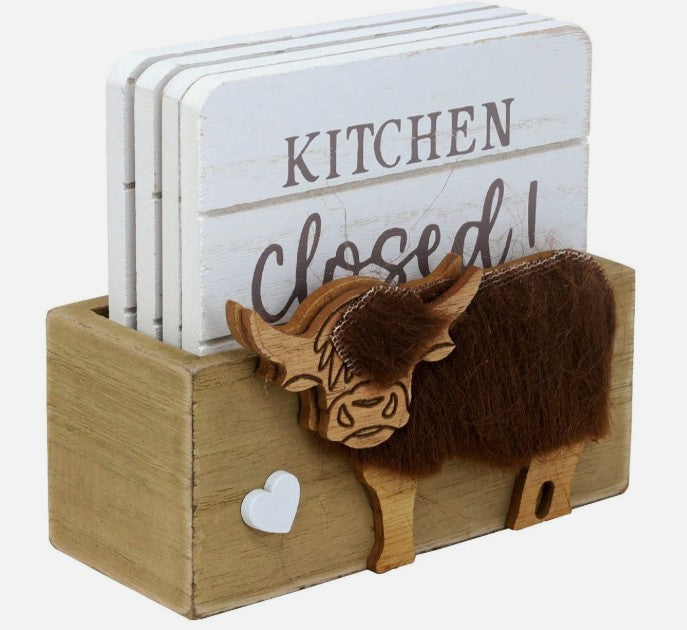 Set of 4 white wooden coasters each with a different slogan, stored in a wooden Highland cow coaster holder, on a white background

