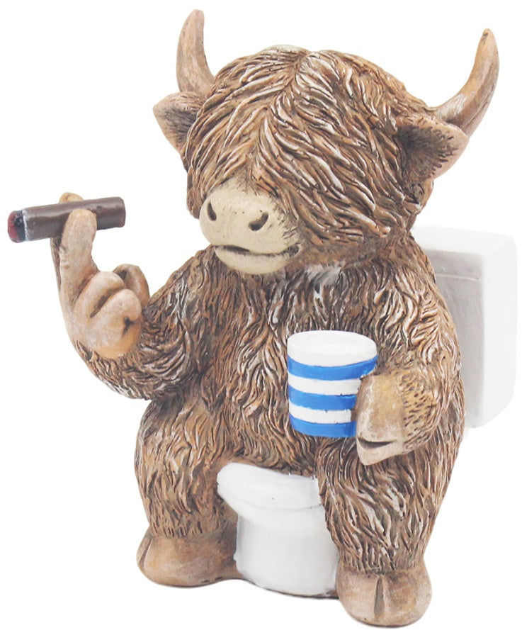 Highland cow figurine sitting on a toilet in a humorous novelty decorative design.