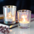 Pair of iridescent glass votive candle holders with sun and moon engravings, lit with tealights and styled with dried flowers and a journal on a white surface