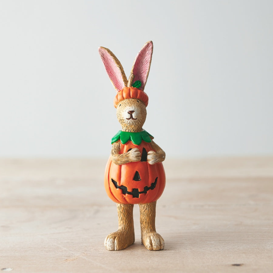 Resin rabbit figurine standing upright wearing a jack-o-lantern pumpkin costume with green collar and pumpkin hat, on a light wooden surface