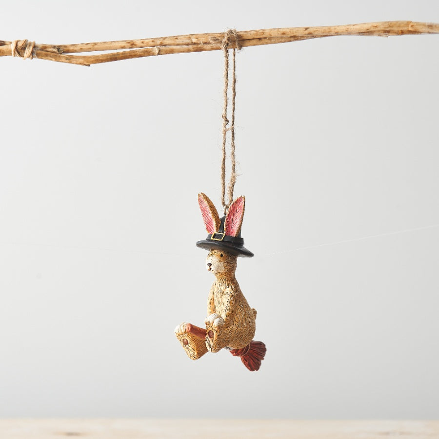 Hanging Halloween decoration featuring Jasper Rabbit wearing a black witch's hat and flying on a broomstick, suspended by rustic twine.
