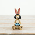 Resin rabbit figurine wearing black gaming headphones and holding a blue game controller, seated on a wooden surface against a neutral background