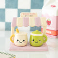 Kawaii ceramic salt and pepper pots shaped like a cream latte cup and green matcha cup with smiley faces, sitting on a pink ceramic Kawaii Kafe stand with a striped awning