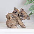 Decorative figurine of a parent koala with a baby koala clinging to its back, featuring textured detailing and a warm, affectionate design.