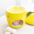 Yellow lemon shaped ceramic oil burner with citrus slice top and lit tealight, styled on a wooden board with wax melts and a fresh lemon