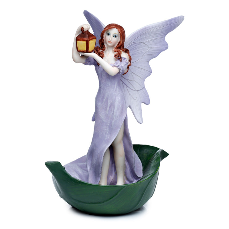 Resin fairy figurine wearing a lilac gown with large delicate wings, holding a glowing lantern aloft, standing on a green leaf base against a white background