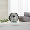 Glass mirrored bee oil burner on white bathroom shelf with grey towels and eucalyptus sprig