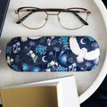Navy hard shell glasses case with a magical night design featuring a white barn owl in flight, blue morpho butterflies, crescent moons, mushrooms, and botanical leaves, styled on a marble tray with tortoiseshell glasses and a book