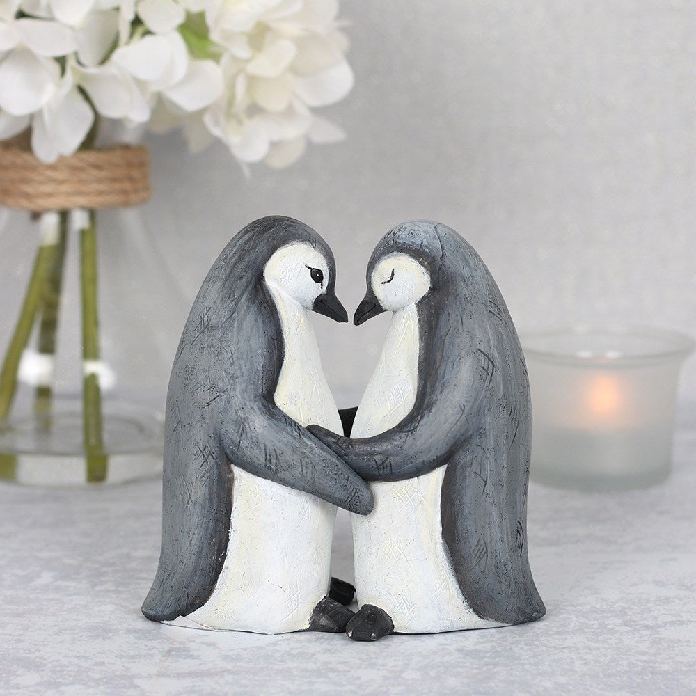 Pair of resin penguin ornaments shown cuddling together with detailed decorative finish symbolising affection and companionship.