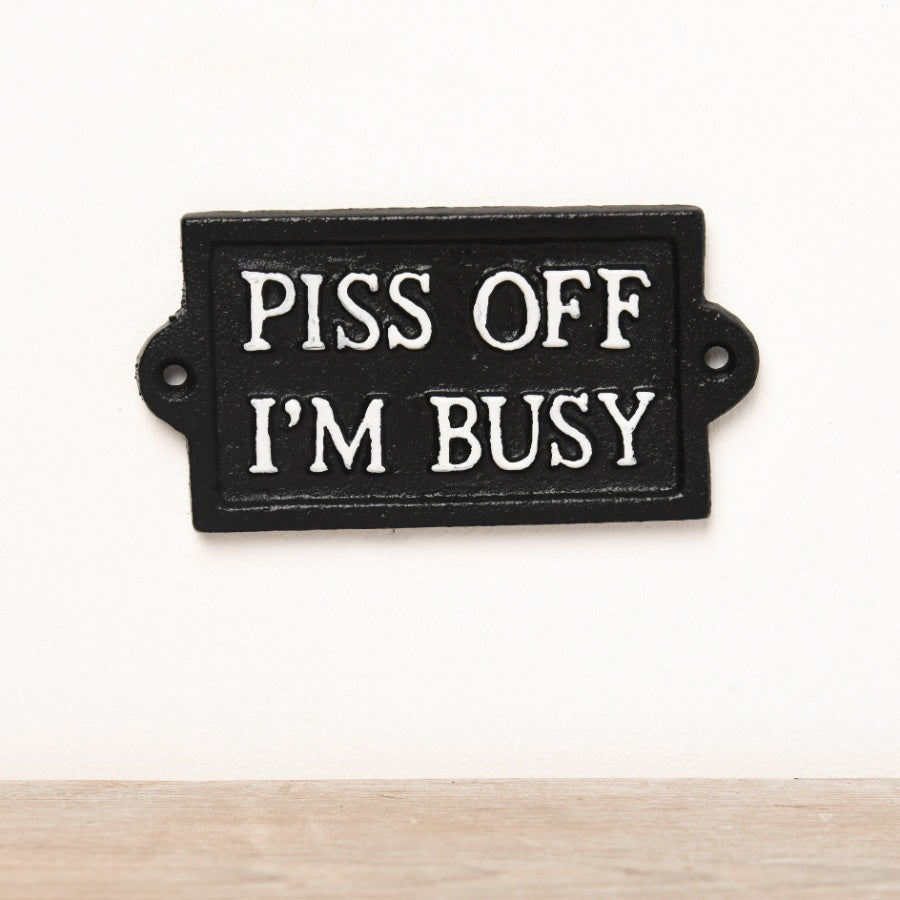 Cast iron wall sign featuring “P*ss Off I'm Busy” text with rustic vintage-style lettering and humorous design.