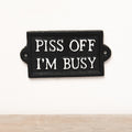 Cast iron wall sign featuring “P*ss Off I'm Busy” text with rustic vintage-style lettering and humorous design.