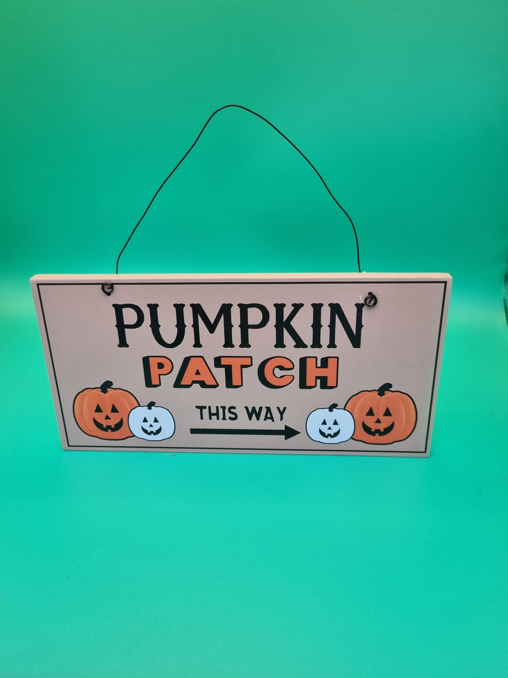 Wooden hanging sign reading Pumpkin Patch This Way with orange and white jack-o'-lantern illustrations and a directional arrow, hung with black wire