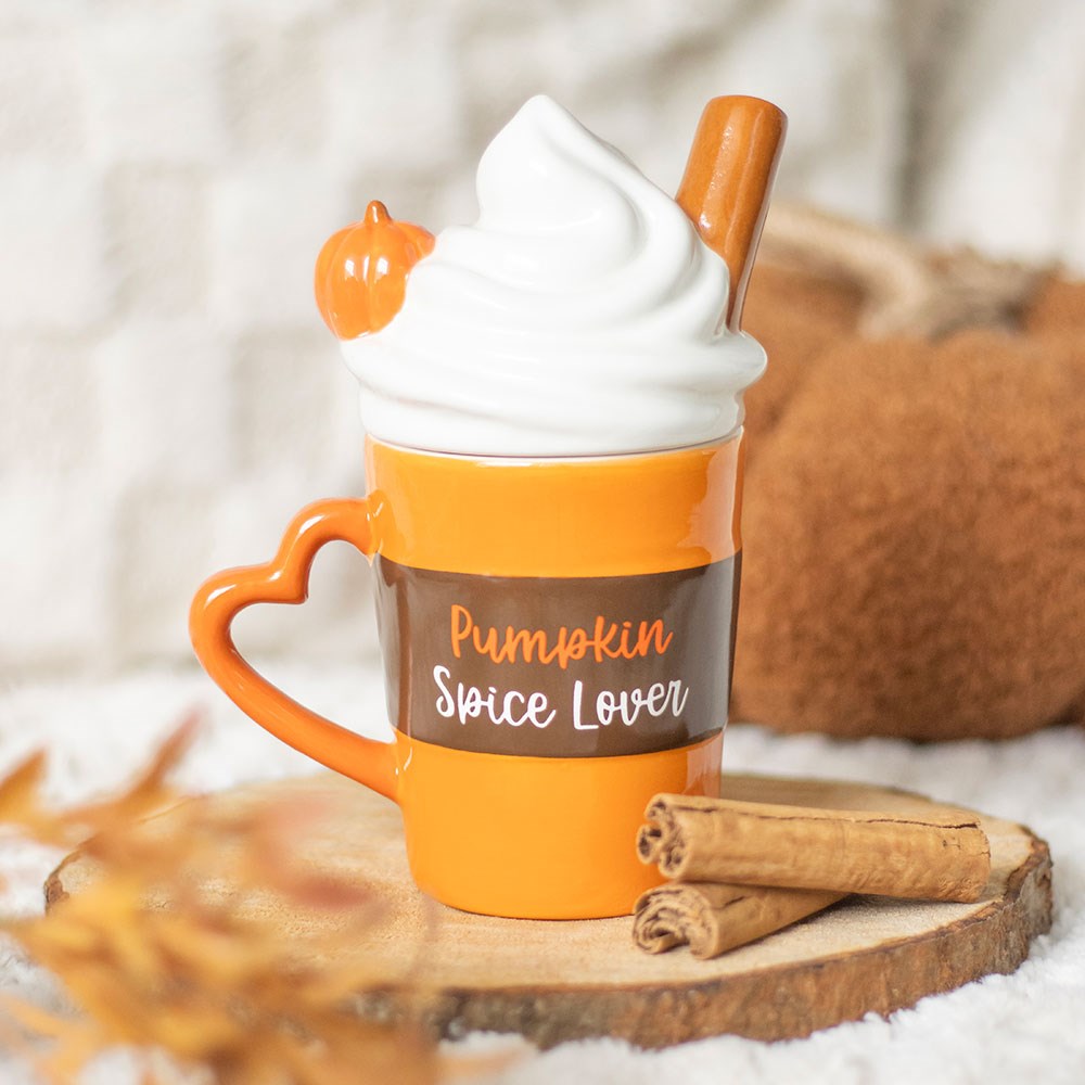 Orange ceramic Pumpkin Spice Lover mug with heart shaped handle and novelty whipped cream lid with cinnamon stick, styled on a wooden slice with cinnamon sticks and autumn leaves