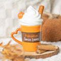 Orange ceramic Pumpkin Spice Lover mug with heart shaped handle and novelty whipped cream lid with cinnamon stick, styled on a wooden slice with cinnamon sticks and autumn leaves