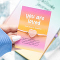 Rose quartz heart bracelet presented with a “You Are Loved” sentiment card and decorative gift-ready design.