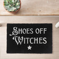 Black coir door mat with Shoes Off Witches slogan in white gothic lettering and a star, styled on a wooden floor with a succulent plant nearby