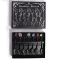 Set of 7 dark silver witch spoons with gemstone crystal handles, mystical themed decorative cutlery arranged together.