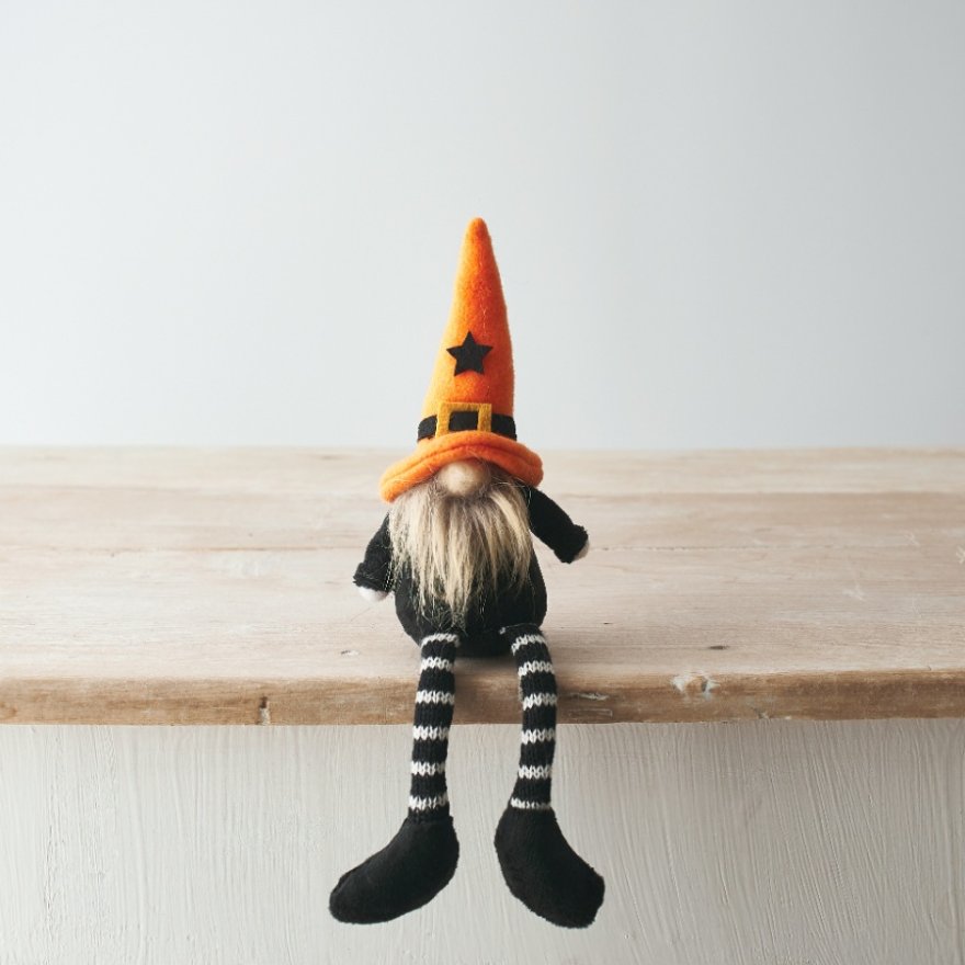 Halloween gonk with orange felt pointed witch hat, white beard, black outfit and black and white striped dangly legs, sitting on the edge of a wooden shelf
