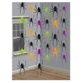 Six foil coloured spider hanging string decorations in black, orange, purple and green, hung from ceiling to floor against a grey wall in a Halloween decorated room