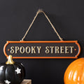 Black and orange hanging metal sign reading "Spooky Street" in silver lettering with twine hanger, on a white background
