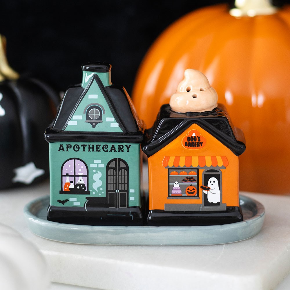 Ceramic Halloween salt and pepper shaker set shaped as a teal apothecary and orange Boo's Bakery building with ghost topper, on a matching tray, white background

