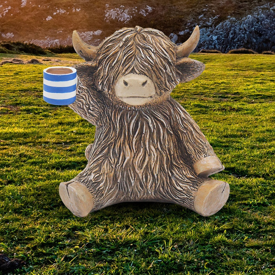 Decorative Highland cow ornament holding a cup of tea with detailed countryside-inspired design and cosy character.
