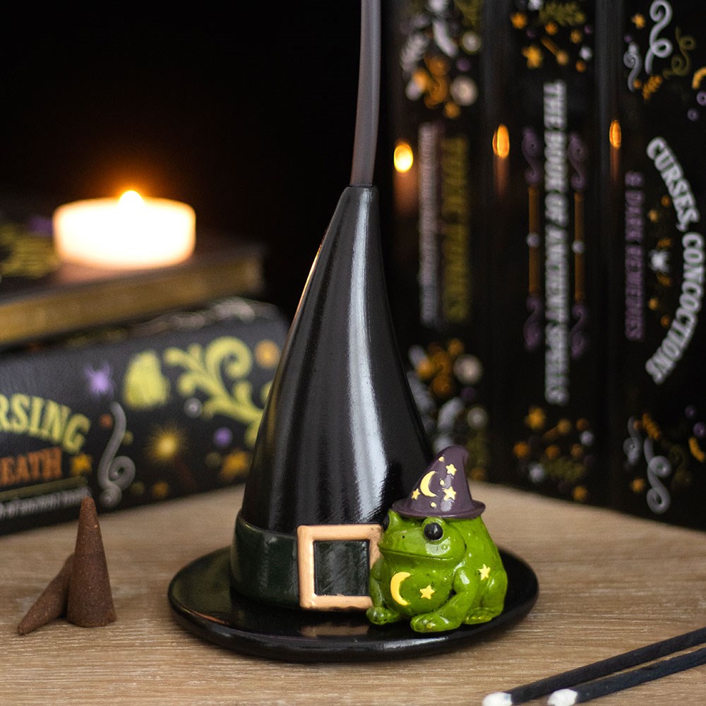 Black resin witch hat incense cone holder with a green magic toad figurine wearing a purple star and moon wizard hat, styled with spell books and a lit candle